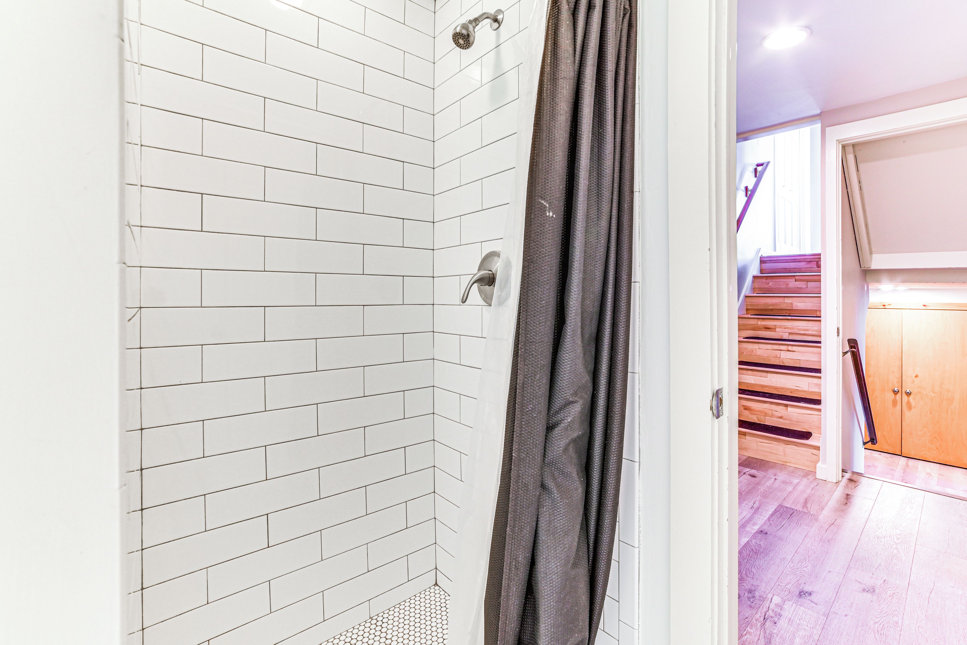 A modern bathroom with white subway tiles, a shower with a glass door, and a wooden staircase leading to a landing.