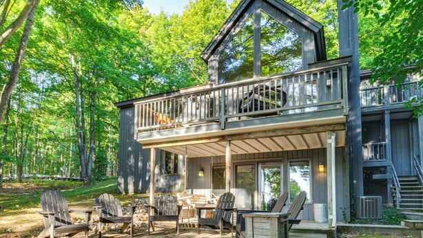 A two-story cabin with a balcony, outdoor seating area, and a fire pit. - Calm in the Woods Fireplace Walk to Town (Suttons Bay)