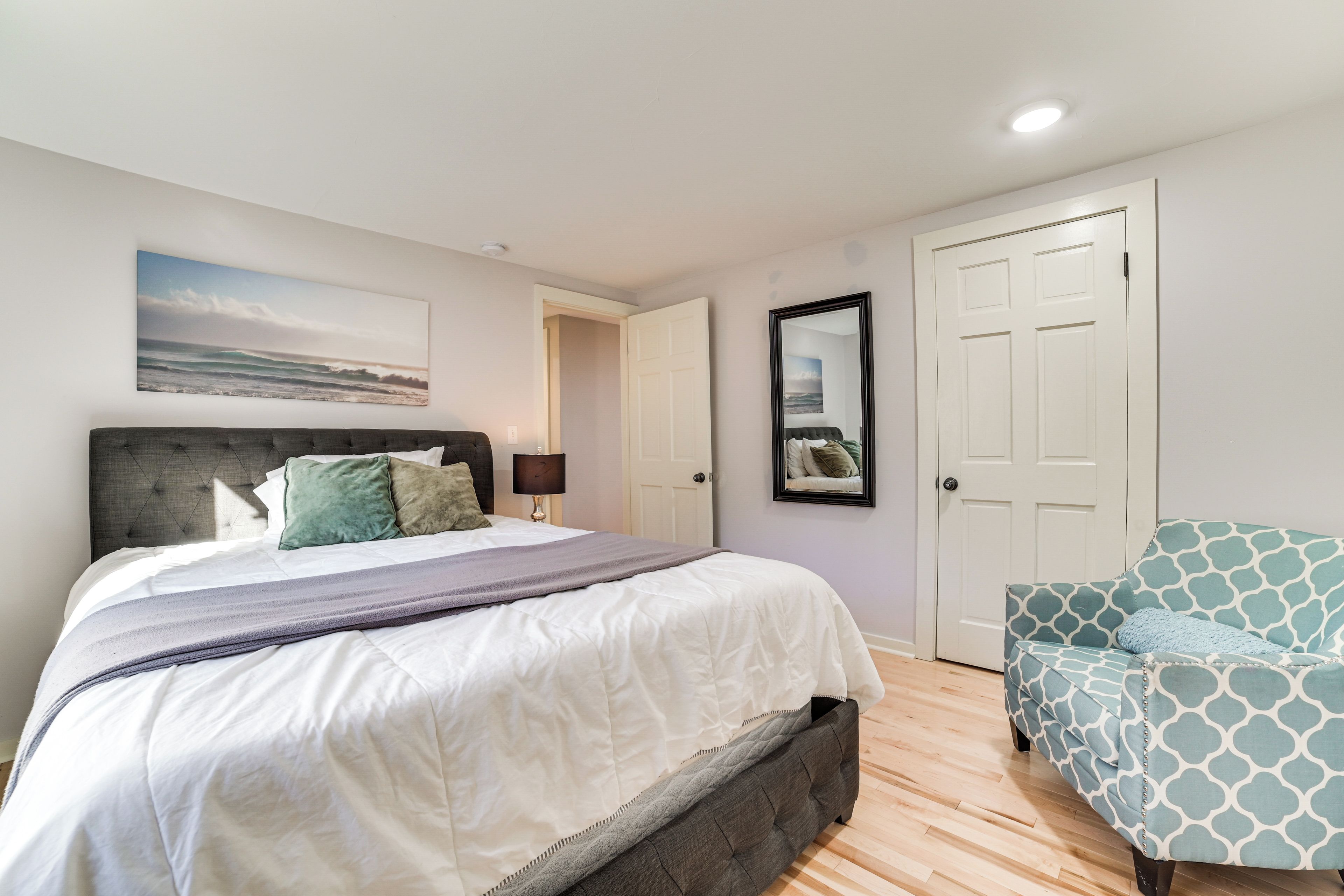 A bedroom with a bed, a nightstand, a lamp, a chair, and a door.
