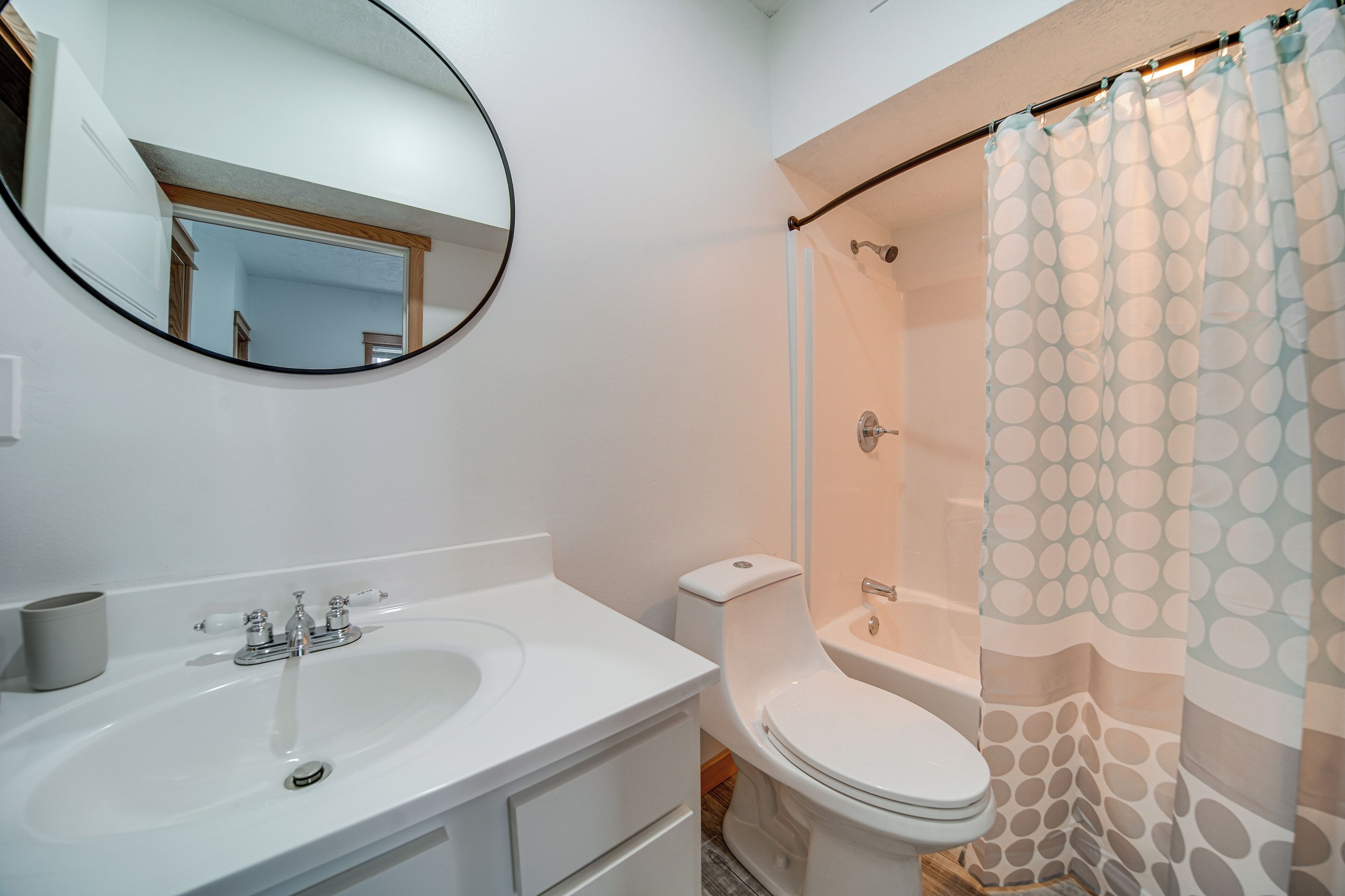 Une salle de bain avec un lavabo blanc, des toilettes, un rideau de douche et un miroir.