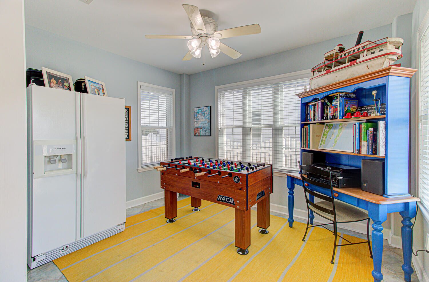 A room with a foosball table, a bookshelf, a desk, and a ceiling fan.