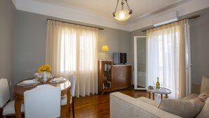 A living room with a sofa, dining table, chairs, and a television. - Le Boulevard (Corfu)