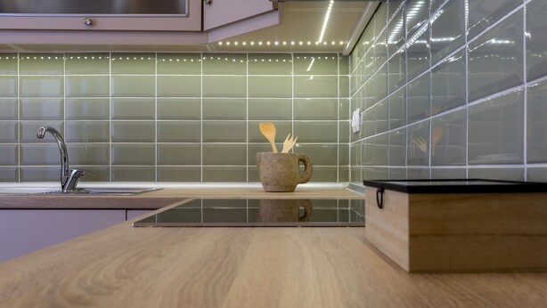 A modern kitchen with a wooden countertop, a built-in sink, and a backsplash with green tiles. - Le Boulevard (Corfu)