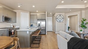 A modern kitchen with stainless steel appliances, a central island with bar stools, and a dining area with a wooden table and chairs. - Crown Point: Ping Pong, Foosball, Hot Tub, Community Pools (Washington)
