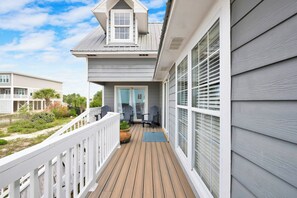 A covered outdoor deck with a railing, a door, and two chairs.