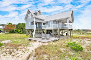 Ein Strandhaus mit Balkon, Treppe und einer sandigen Umgebung.