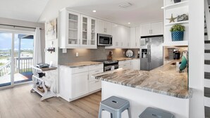 A modern kitchen with white cabinetry, a marble countertop, and a view to the outside. - Pet Friendly | Gulf Views | Golf Cart | Deeded Beach Access (Gulf Shores)