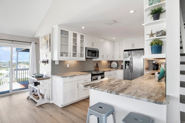 A modern kitchen with white cabinetry, a marble countertop, and a view to the outside. - Pet Friendly | Gulf Views | Golf Cart | Deeded Beach Access (Gulf Shores)