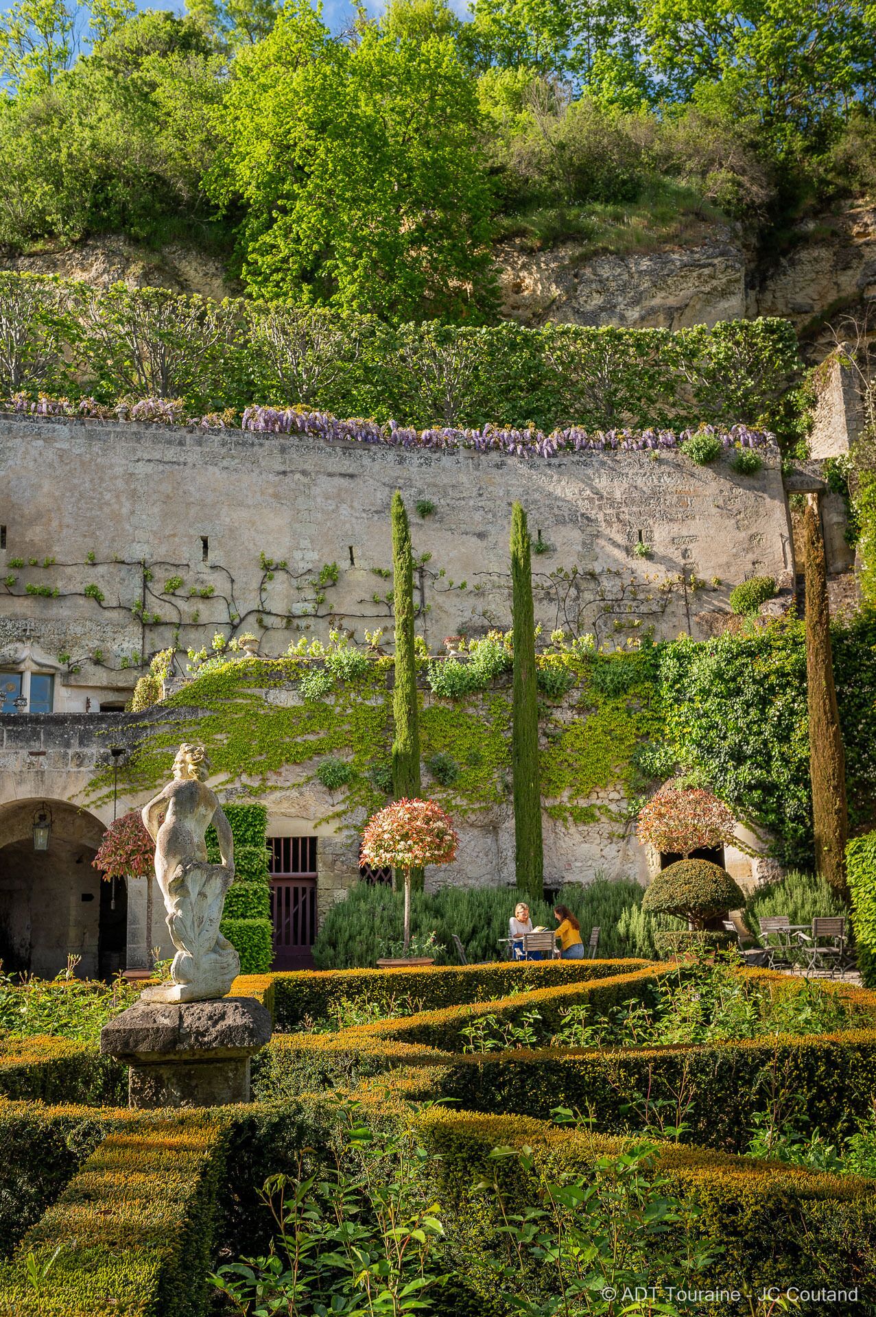 A garden with a statue, neatly trimmed hedges, and a stone wall.
