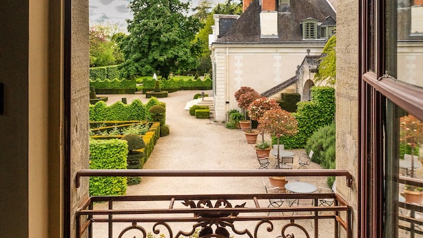 A view through an arched window of a garden with a pathway, a building, and a metal railing. - MANOIR DES BASSES RIVIERES (Rochecorbon)