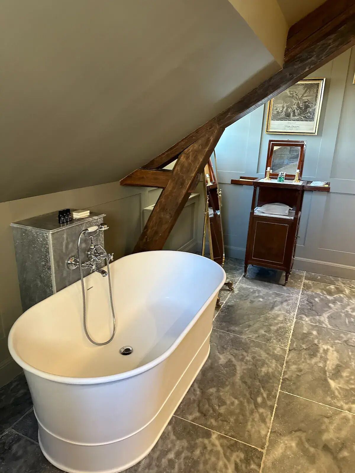A bathroom with a freestanding bathtub, a wooden staircase, a vanity with a mirror, and a framed picture on the wall.