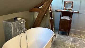 A bathroom with a freestanding bathtub, a wooden staircase, a vanity with a mirror, and a framed picture on the wall.