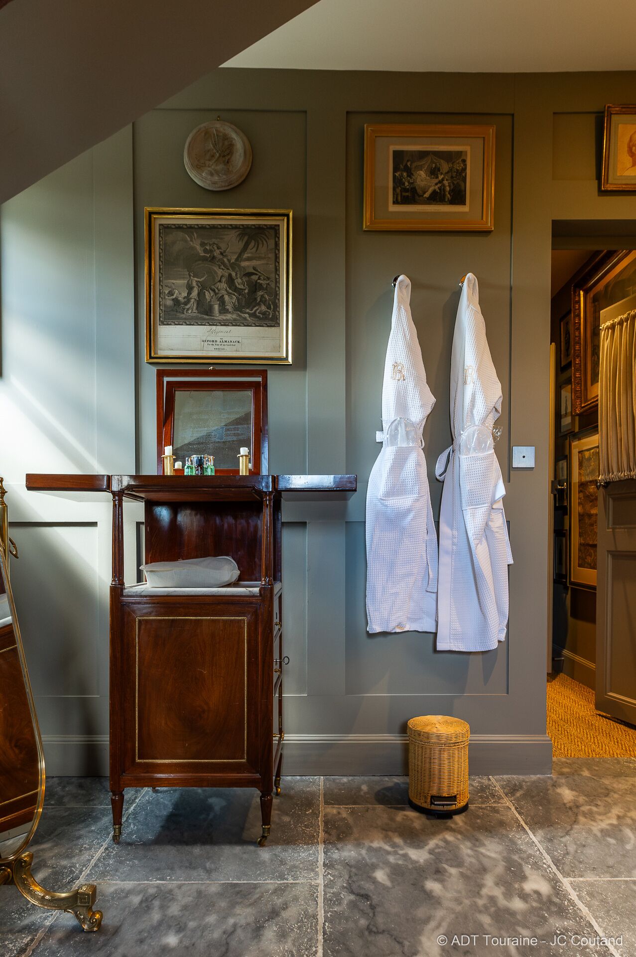 A bathroom with a wooden vanity, a mirror, and two white robes hanging on the wall.