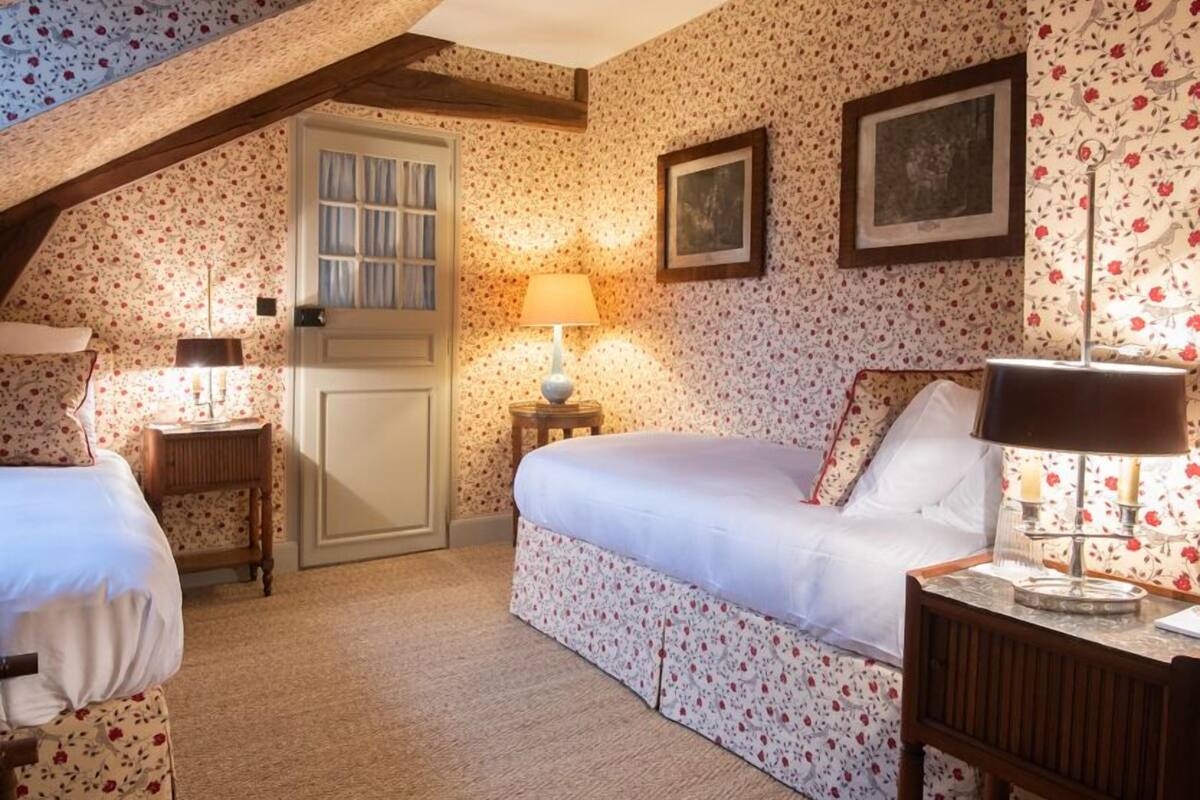 A bedroom with floral wallpaper, a wooden door, two bedside tables with lamps, and a bed.