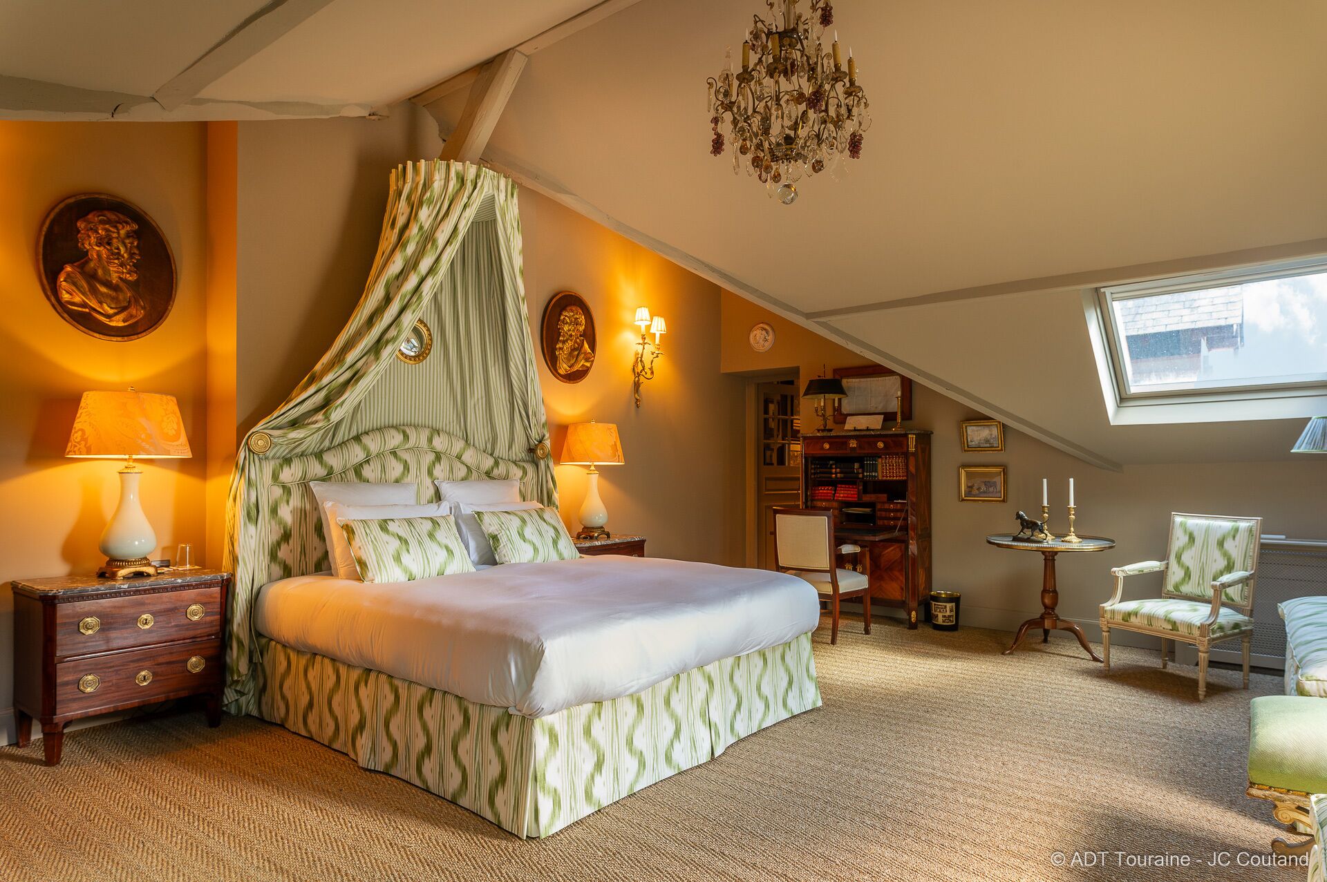 Une chambre à coucher avec un lit à baldaquin, un lustre et une vue sur le ciel grâce à une lucarne.