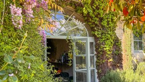 A garden with a glass greenhouse structure, surrounded by lush greenery and flowering plants. - MANOIR DES BASSES RIVIERES (Rochecorbon)