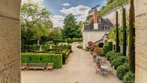 A courtyard with a gravel path, benches, and tables, surrounded by well-manicured hedges and trees. - MANOIR DES BASSES RIVIERES (Rochecorbon)