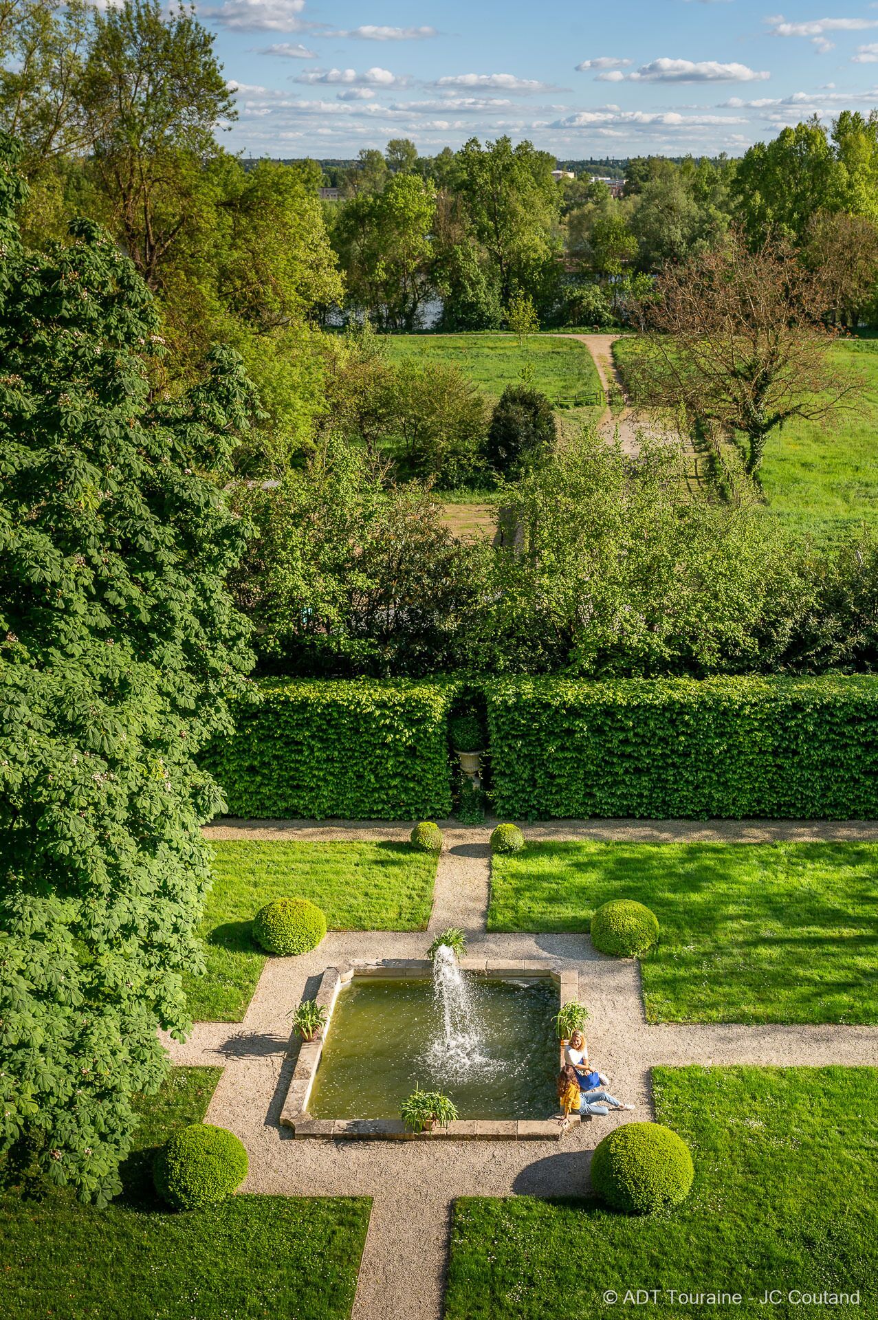 Een tuin met een centrale fontein, verzorgde hagen en een duidelijk pad.