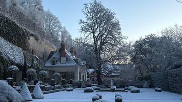 A snow-covered garden with a house, trees, and snow-covered bushes.