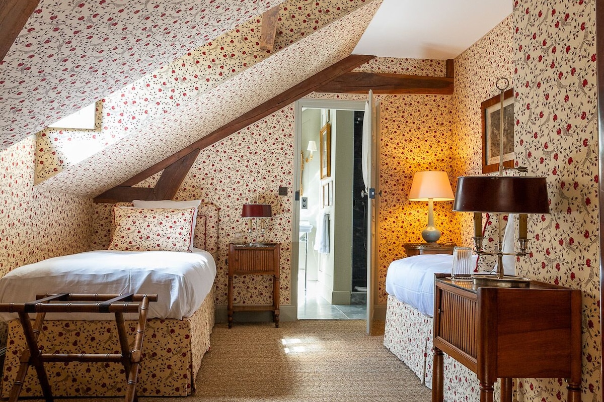 A bedroom with two beds, a wooden table, a mirror, and a lamp.