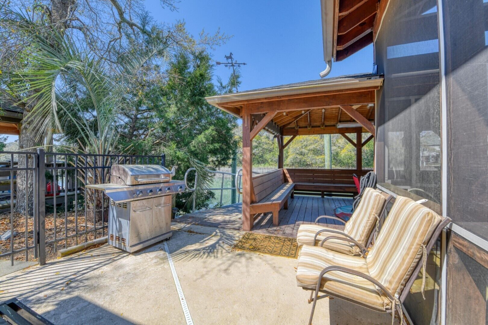 Un patio al aire libre con una parrilla, un banco de madera y una zona de estar cubierta.
