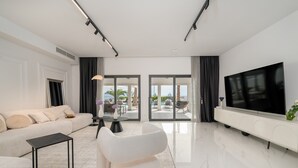 A modern living room with a sofa, a coffee table, a TV, and a view of the outdoors through large glass doors.