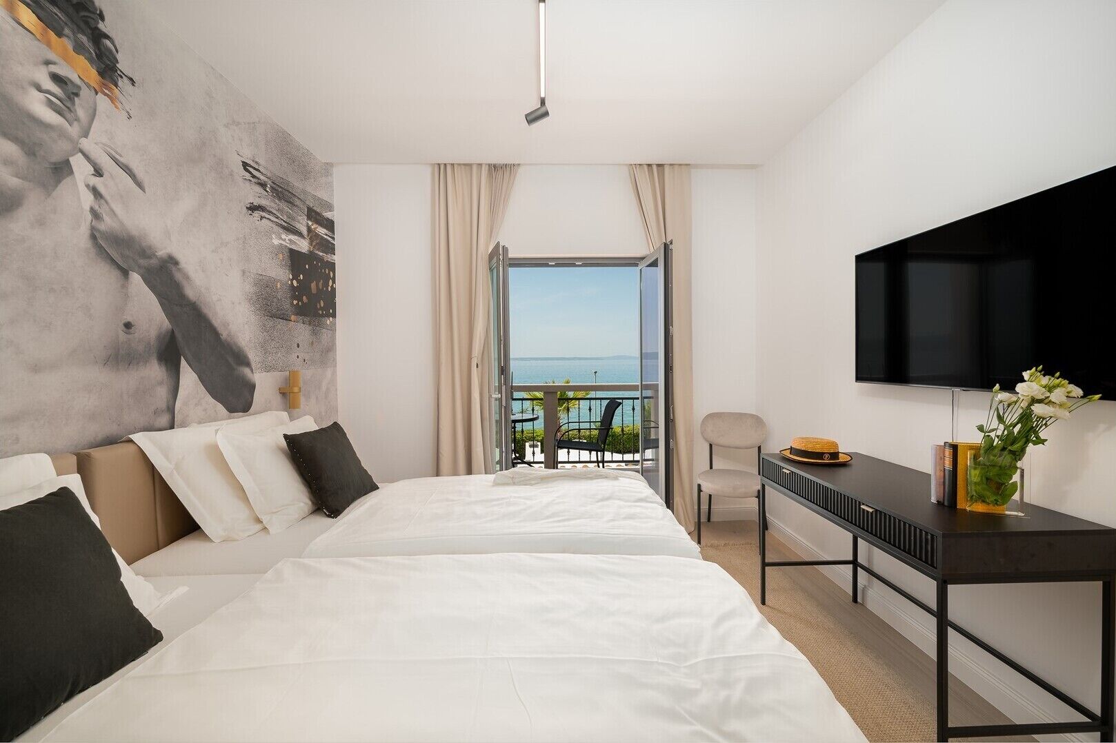 Une chambre d’hôtel moderne dotée d’un grand lit, d’un bureau avec un téléviseur à écran plat et d’un balcon offrant une vue sur la mer.