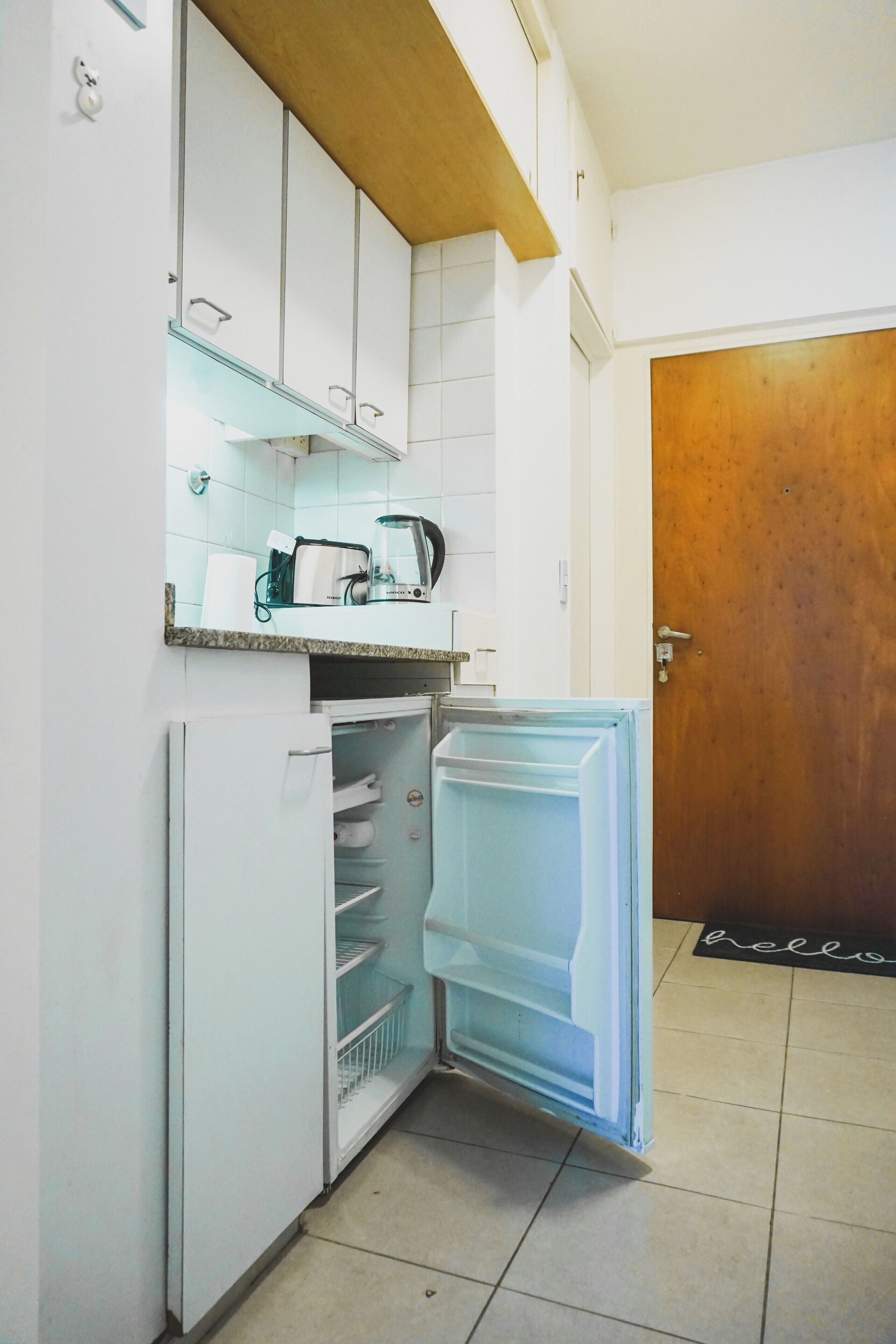 Cuina compacta amb armaris blancs, un taulell amb una papereta i un refrigerador amb la porta oberta.
