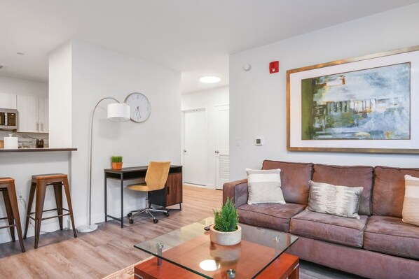Un appartement moderne comprenant une cuisine, un coin repas, un salon avec un canapé et une table basse, ainsi qu’un grand tableau accroché au mur.