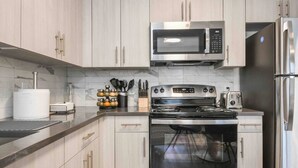A modern kitchen with light wood cabinets, stainless steel appliances including a microwave, oven, and refrigerator, and a marble backsplash. - Vibrant Studio KING ! Free Parking ! 30 min to NYC (Orange)