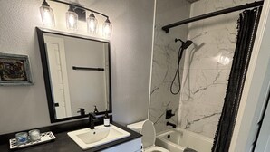 A bathroom with a white sink, a toilet, and a shower area. - Ranch Hand Cabin in Llano Texas  (Llano)