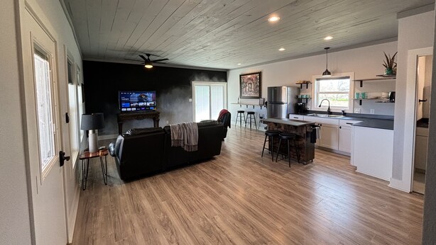A spacious living area with a dark-colored sofa, a television, and a kitchen area with a refrigerator and sink. - Ranch Hand Cabin in Llano Texas  (Llano)