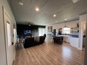 A spacious living area with a dark-colored sofa, a television, and a kitchen area with a refrigerator and sink. - Ranch Hand Cabin in Llano Texas (Llano)
