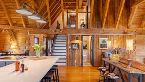 A spacious kitchen with a large island, wooden beams, and a view to the upper level.
