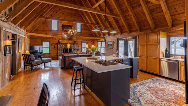 A spacious kitchen with a large island, wooden beams, and a stone fireplace.