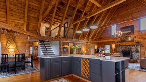 A spacious kitchen with a large island, wooden beams, and a stone fireplace.