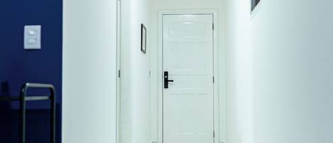 A narrow hallway with white walls, a blue accent wall, a white door at the end, and a small potted plant.