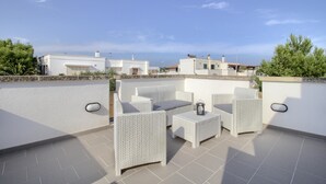 A rooftop terrace with white wicker furniture, a small table, and a lantern.