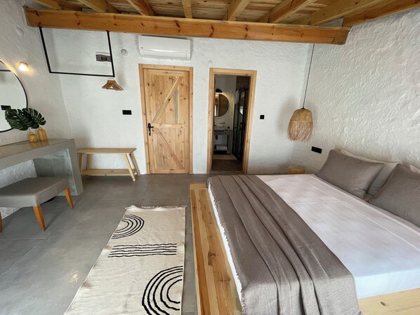 A bedroom with a bed, bedside table, and a bench. There is a door leading to a bathroom and a hallway.