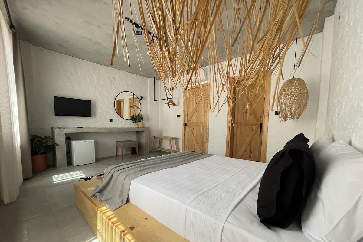 A modern bedroom with a wooden bed, a desk, a chair, a television, and a mirror.