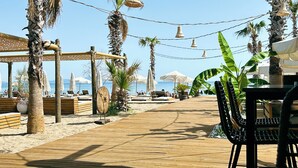 Un patio frente a la playa con piso de madera, palmeras y luces colgantes.