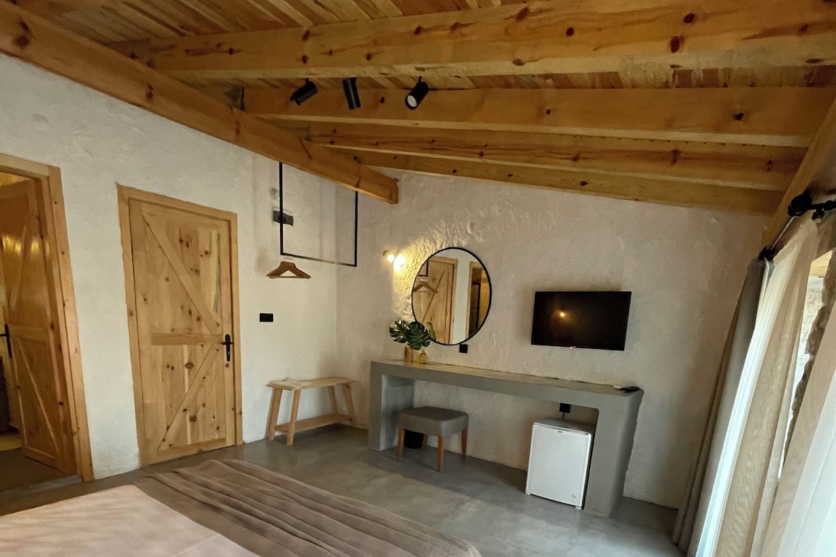 A bedroom with a wooden ceiling, a bed, a desk, a chair, a mirror, and a television.