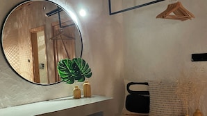 Un baño moderno con un espejo redondo, un banco de madera y un estante con una planta y una radio.