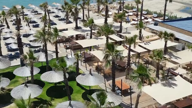 Un resort con múltiples sombrillas en la playa, palmeras y vista al océano.
