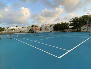 Un court de tennis avec un filet, entouré d’immeubles et d’arbres.