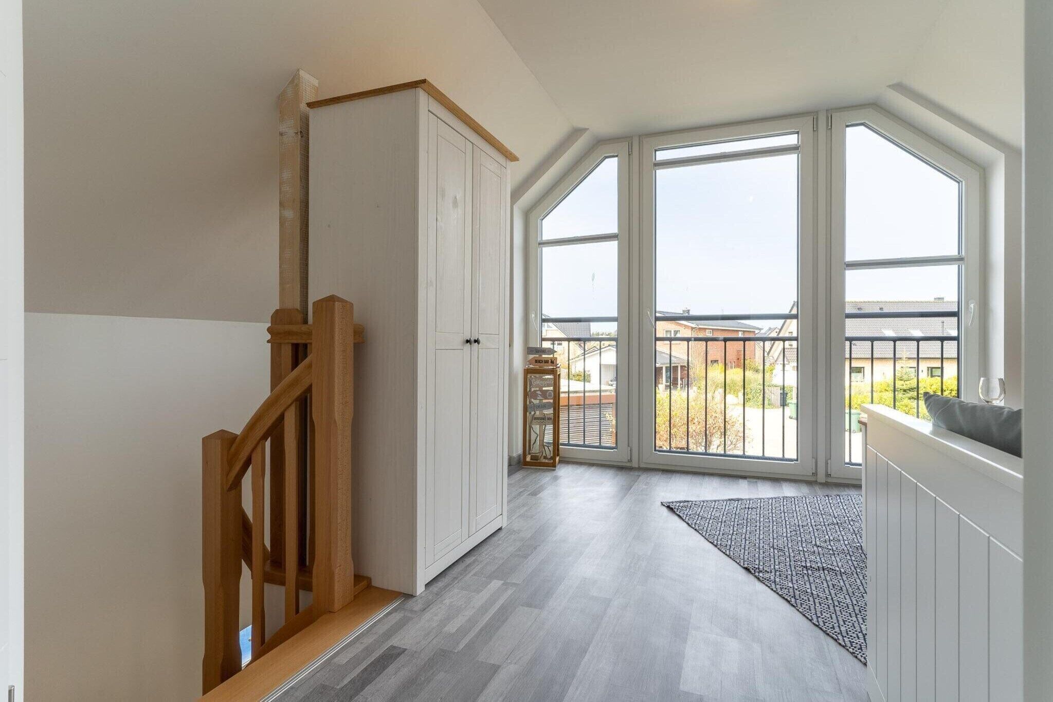 A spacious room with a wooden staircase, a large sliding glass door leading to a balcony, and a view of the outside.