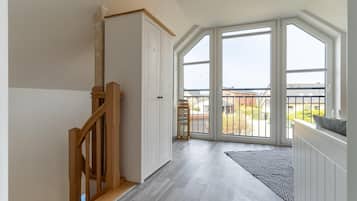 A spacious room with a wooden staircase, a large sliding glass door leading to a balcony, and a view of the outside.