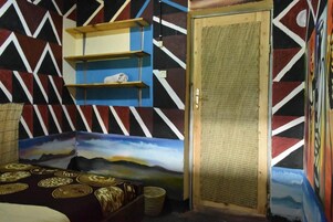 A room with a geometric-patterned wall, a door with a textured panel, and a bed with patterned bedding.