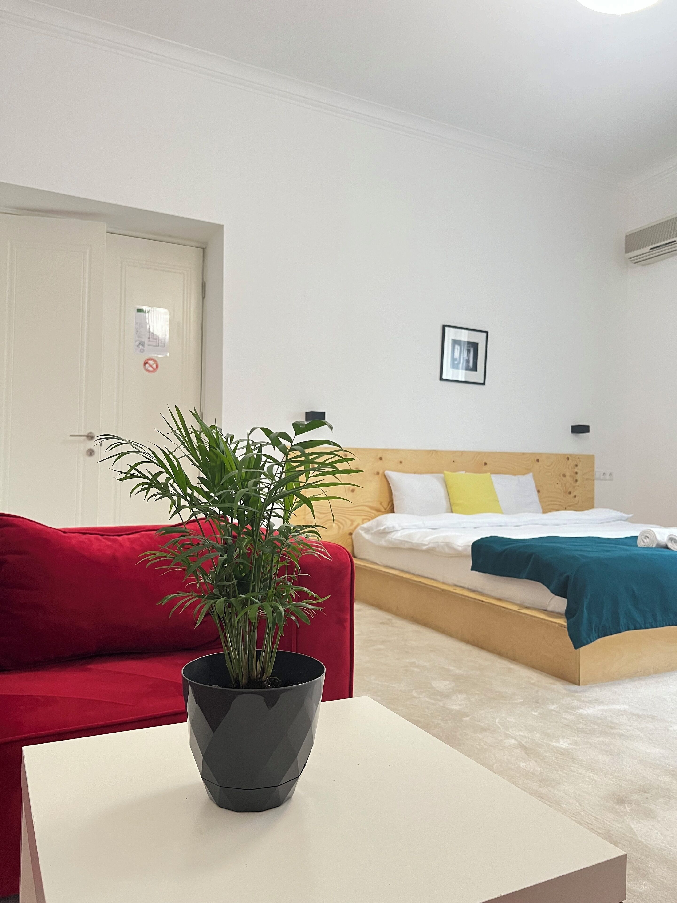 A room with a bed, a red couch, a small table, and a potted plant.