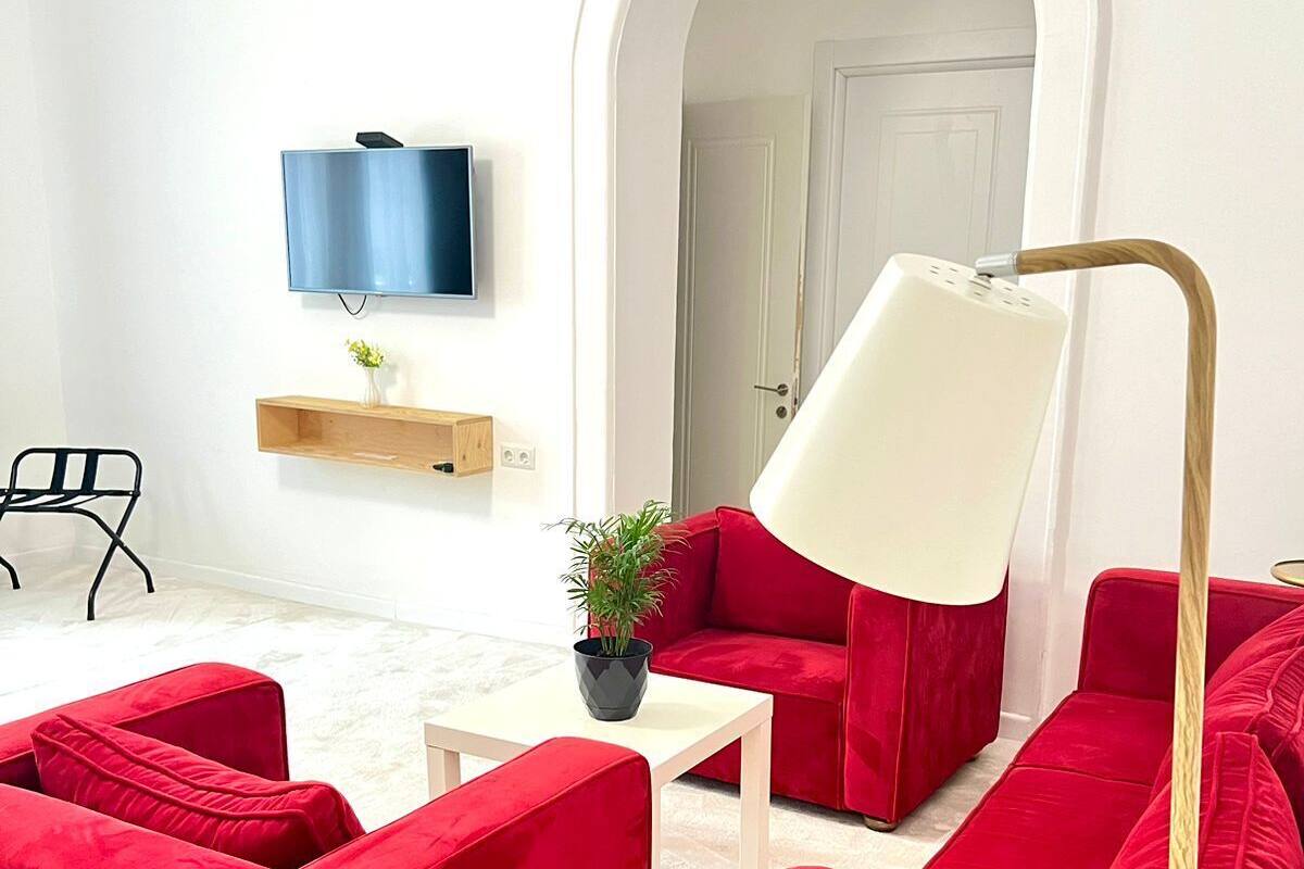A modern living room with red sofas, a white coffee table, a floor lamp, a TV, and a plant.